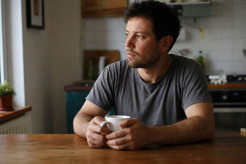 Thoughtful man sitting at kitchen table holding coffee mug representing male infertility awareness